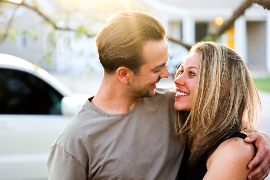 A happy couple stands in front of a beautiful house, smiling and holding up a set of keys, representing a successful real estate transaction and financial savings.