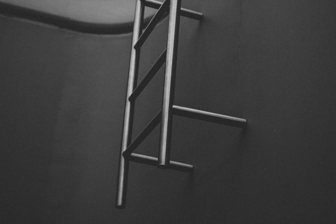 A modern, minimalist ladder leans against a clean, bright wall but doesn't reach the top, representing the limitations and plateaus of the traditional corporate ladder.