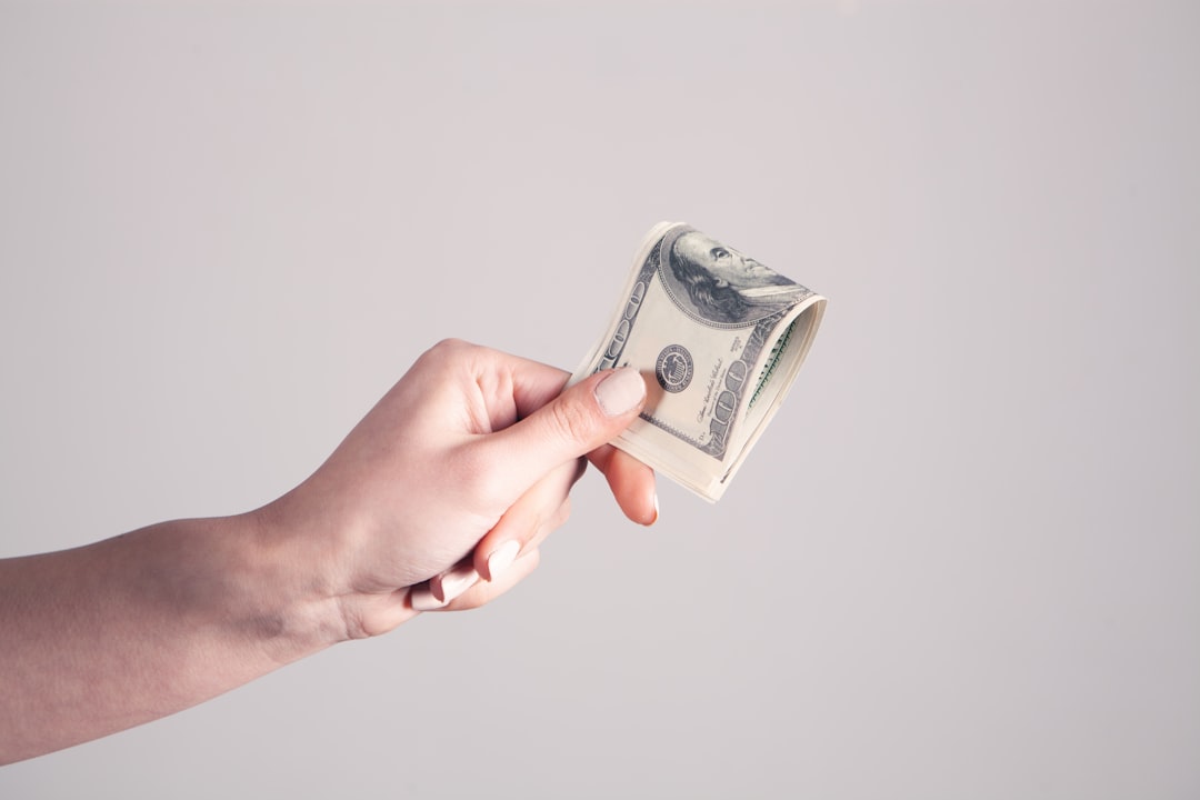 A close-up shot of a person's hands carefully placing dollar bills into a clear glass jar labeled 'Emergency Fund,' highlighting the importance of having cash accessible.