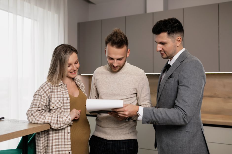 A professional real estate agent and a client sit at a table in a modern, sunlit home, collaboratively reviewing plans on a tablet.